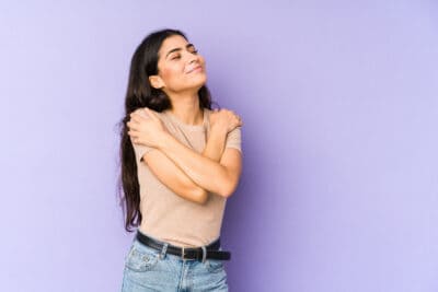 A young women with long hair crossing her arms in front of her body and giving herself a hug.