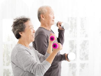 An older couple demonstrating exercises for seniors at home with bicep curl,