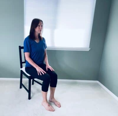 A woman seated in a char neat a window in chair pose mountain pose with a long spine.