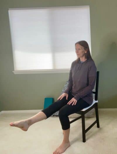 A women seated in a chair with one leg extended and pointing her toes for an ankle pumps exercises.