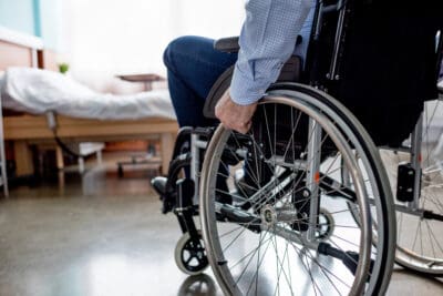 A cropped picture of an older man propelling a wheelchair in a hospital room.