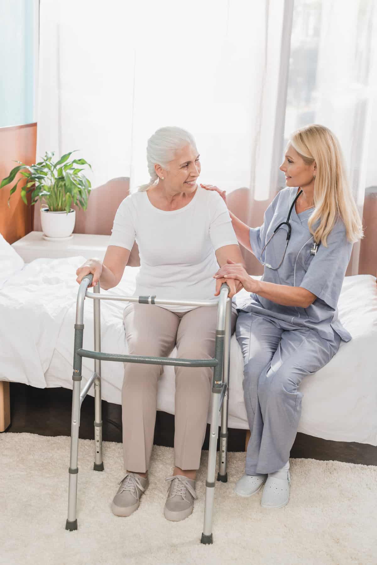 A older women with a walker sitting on a bed next to a nurse discussing safety for seniors at home prior to a discharge home.