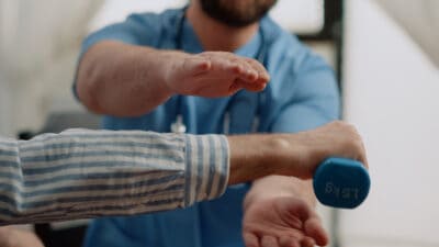 Close up and cropped image of an older women holding a dumbbell exercise with a physical therapist