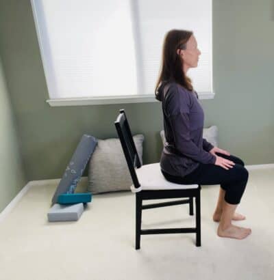 A woman seated in a chair with her back slightly arched in chair yoga cow pose.