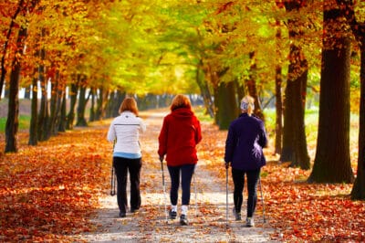 Three woman walking with walking poles on a path among autumn colored trees.