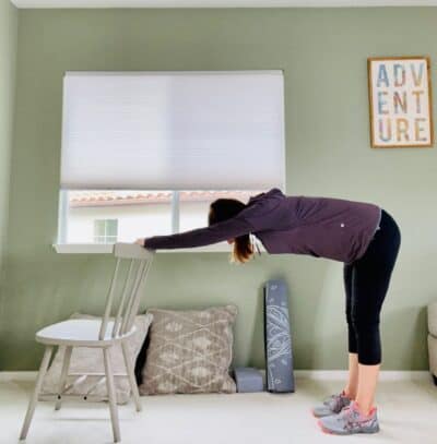 A woman practicing downward facing dog using a chair for modification.