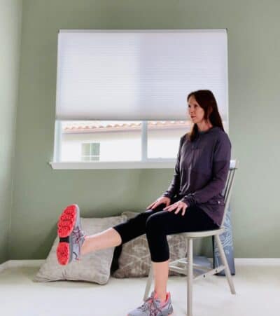 A woman seated in a chair for chair yoga with one knee extended.