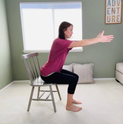 A woman practicing a chair yoga chair pose with arms reaching forward.