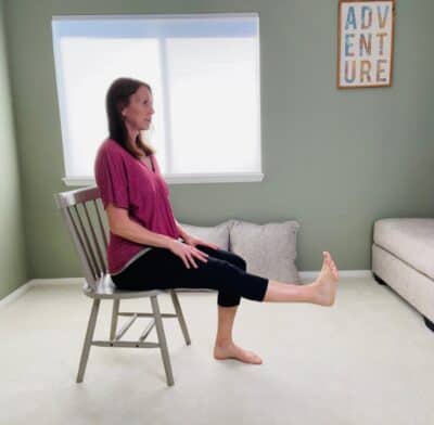 A woman seated in a chair for chair yoga with one knee extended.