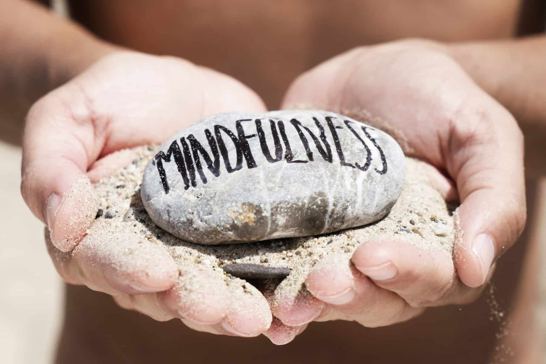 A close up of a woman's hands holding a rock that says mindfulness as a mindfulness exercise.