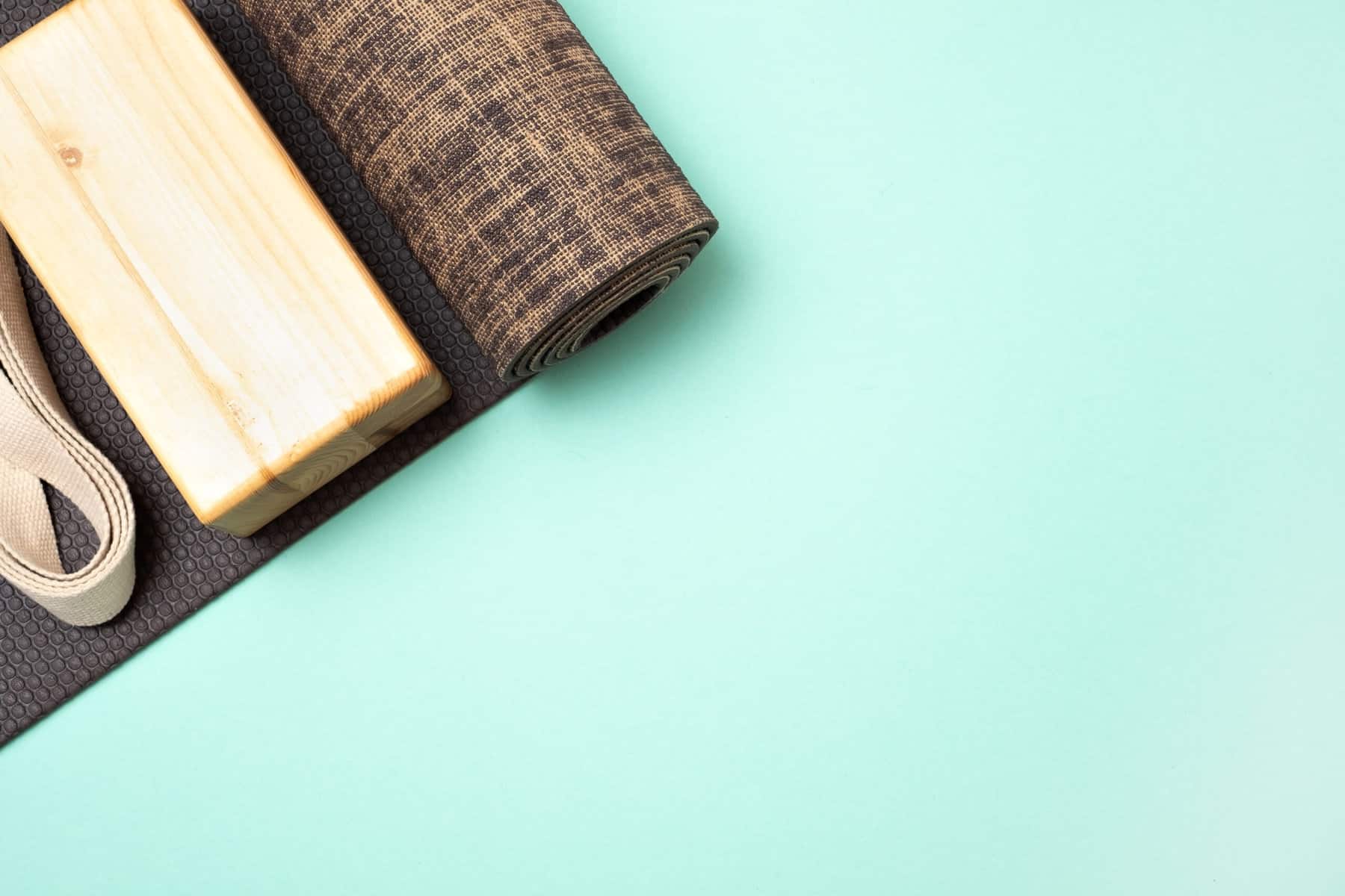 An aqua blue background with a cropped photo of a brown yoga mat and a light brown yoga block.