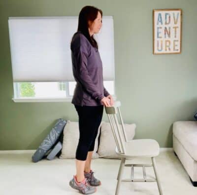 A woman holding a chair for support as she lifts her toes off the ground and rises up onto her heels.