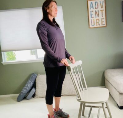 A woman practicing a modified upward facing dog while holding a chair for support as she arches her back.