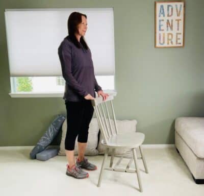 A woman practicing chair yoga mountain pose while holding a chair for support.