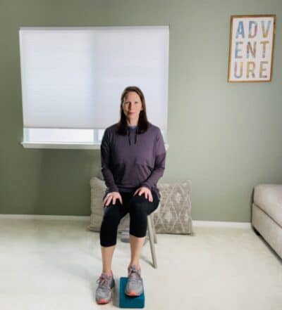 A woman seated in a chair with one foot placed on top of a yoga block.