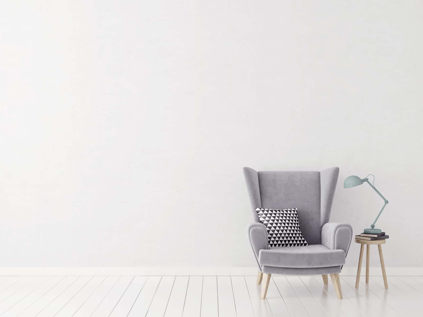 A gray upholstered chair with a gray pillow in a room with white walls and white wood floor.