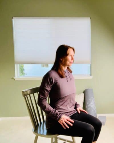 A woman seated in a chair with her shoulders back for chair yoga exercise shoulder circles.