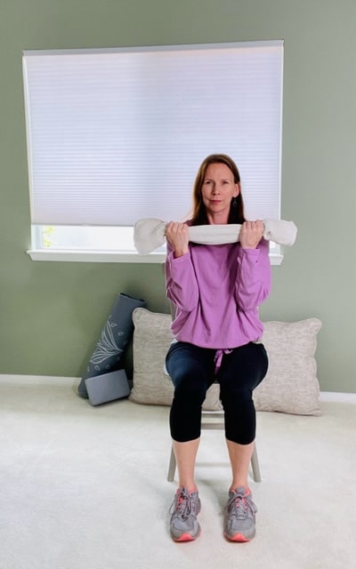 A woman holding the ends of a rolled towel with elbows bent for a bicep curl exercise.