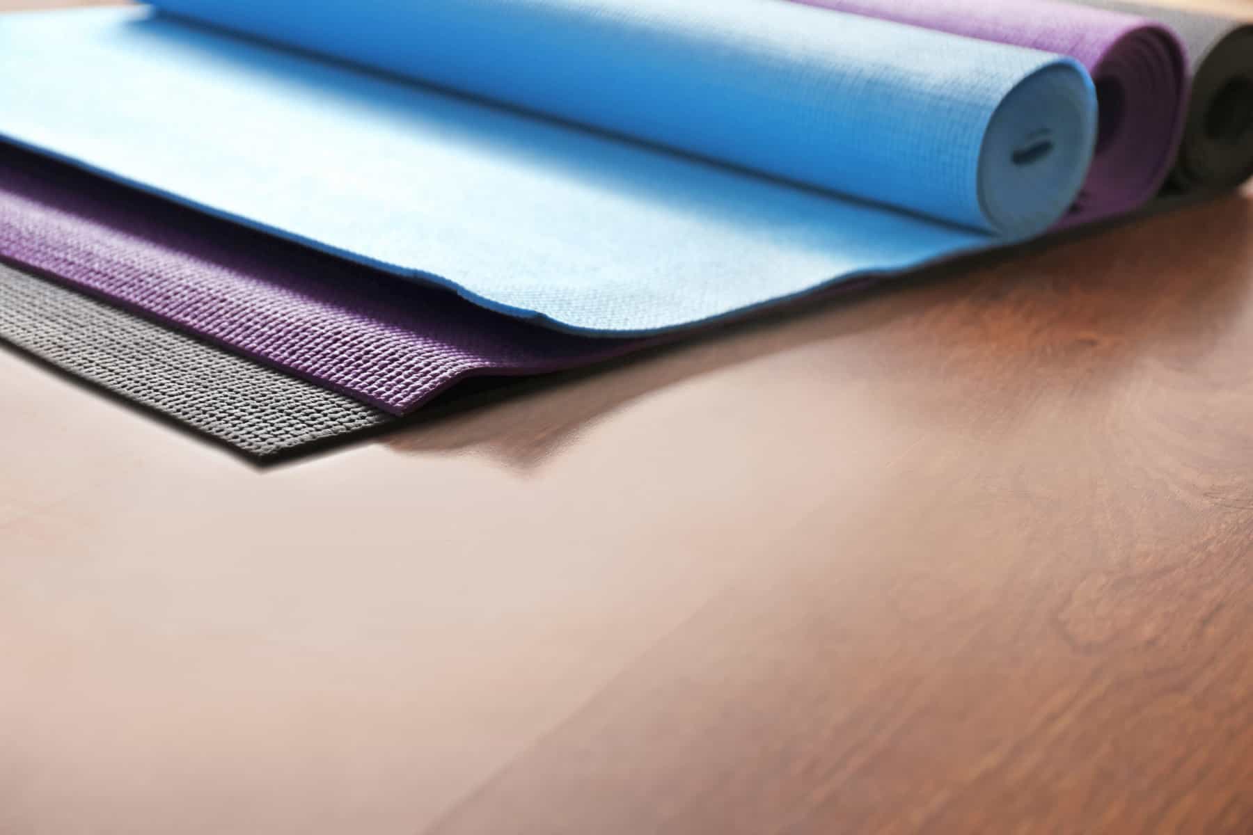 A cropped image of a wooden floor with three yoga mats partially unrolled gathered together.