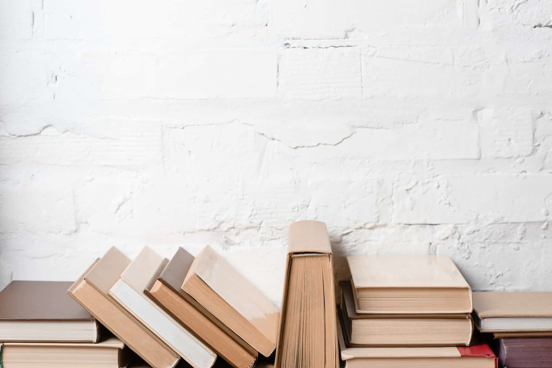 A stack of books piled up in front of a white brick wall.