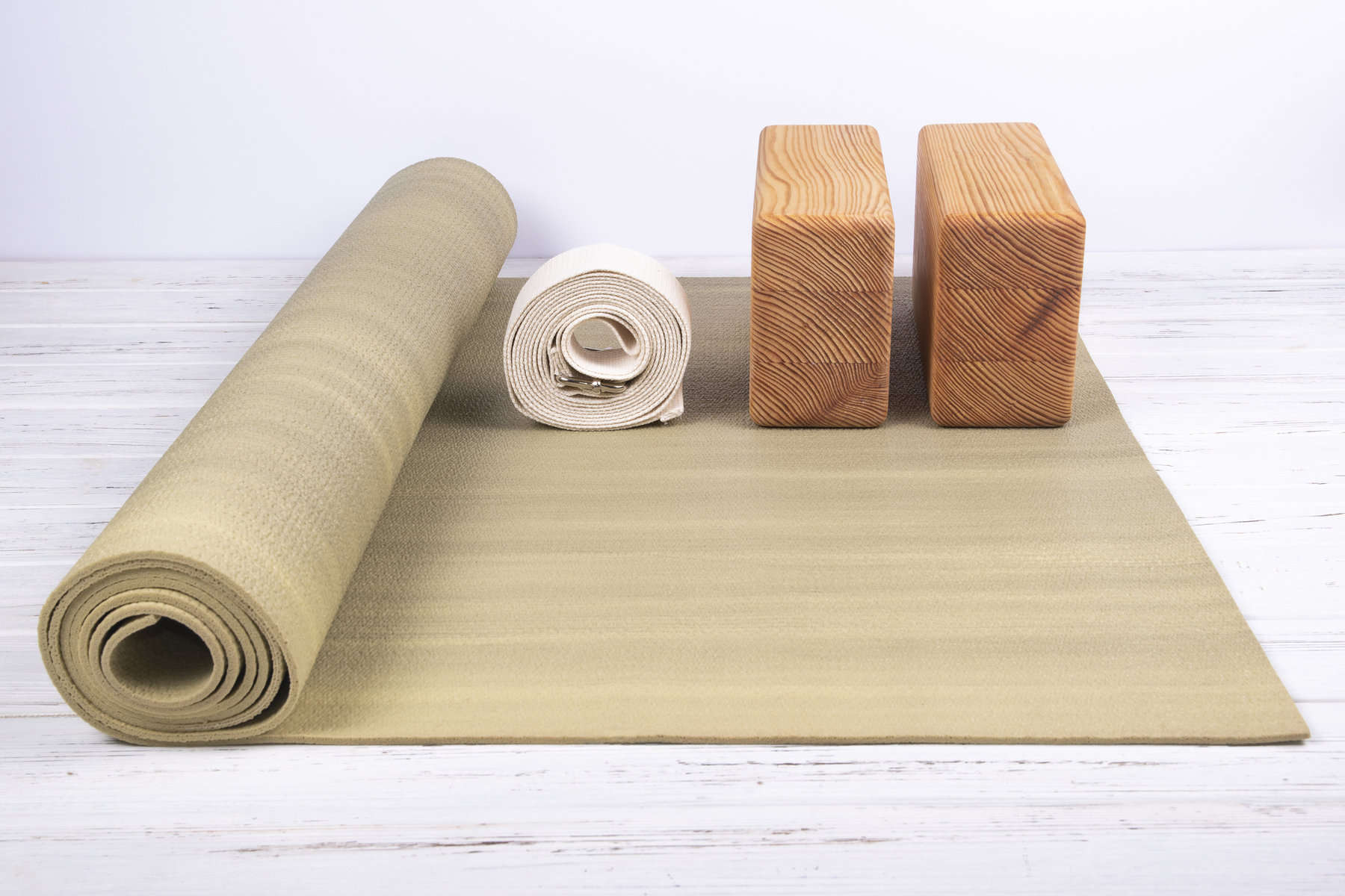 A light brown yoga mat rolled up halfway with two brown yoga blocks and a beige yoga strap placed on top.