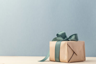 A small gift box wrapped in brown paper with a green bow against a blue backdrop.