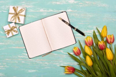 A blank open notebook on a blue wooden table with a pen and a bunch of tulips.