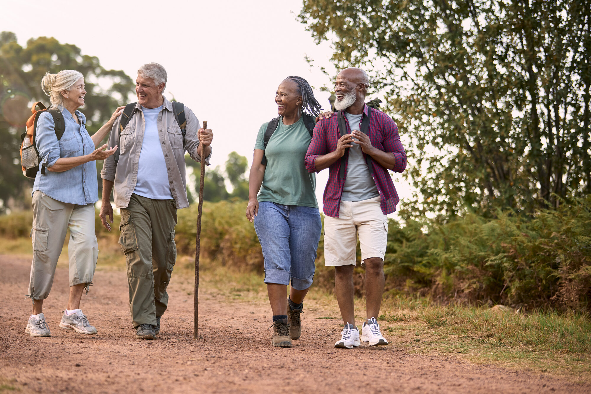 A group of four older adults walking on a path surrounded by trees.