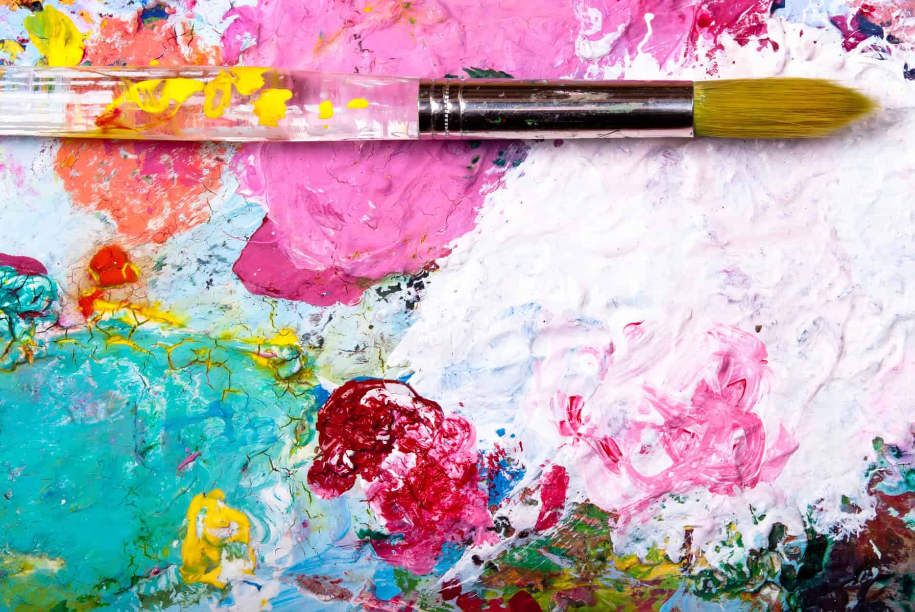 A paintbrush on a canvas background with multiple paint color splashes.