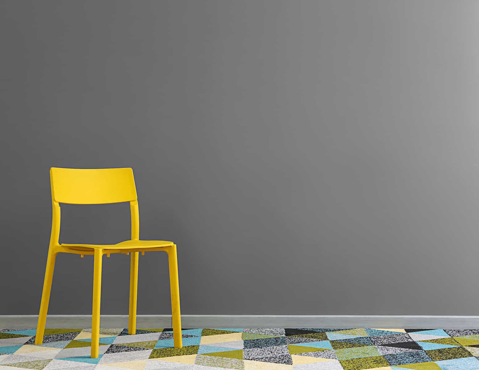 A yellow chair near a gray wall on a patchwork pattern floor.